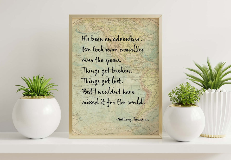 a high quality art print featuring an Anthony Bourdain quote. the print has a vintage map background and is displayed in a gold frame. The frame is plced between some small potted plants. 