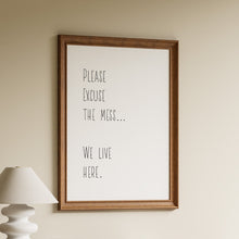 Load image into Gallery viewer, Please excuse the mess, we live here, in tall black minimalist lettering on a white background in a wooden frame