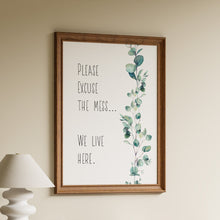 Load image into Gallery viewer, Please excuse the mess, we live here, in black hand-lettered text with watercolour eucalyptus on a white background in a wooden frame