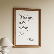 Load image into Gallery viewer, What you seek is seeking you, Rumi quote in black handwritten script on a white background in a wooden frame