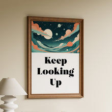 Load image into Gallery viewer, A framed wall art print hanging above a wooden shelf in a styled interior. The print features an abstract sky illustration in teal, cream, and coral tones above the text 'Keep Looking Up' in black serif lettering on a white background.

