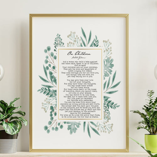 May include: A framed print with a gold frame and a white background. The print features a poem titled 'On Children' by poet John Greenleaf Whittier. The poem is surrounded by a watercolor illustration of green leaves and flowers. The print is displayed on a wooden shelf with two green plants and two light bulbs hanging from the ceiling.